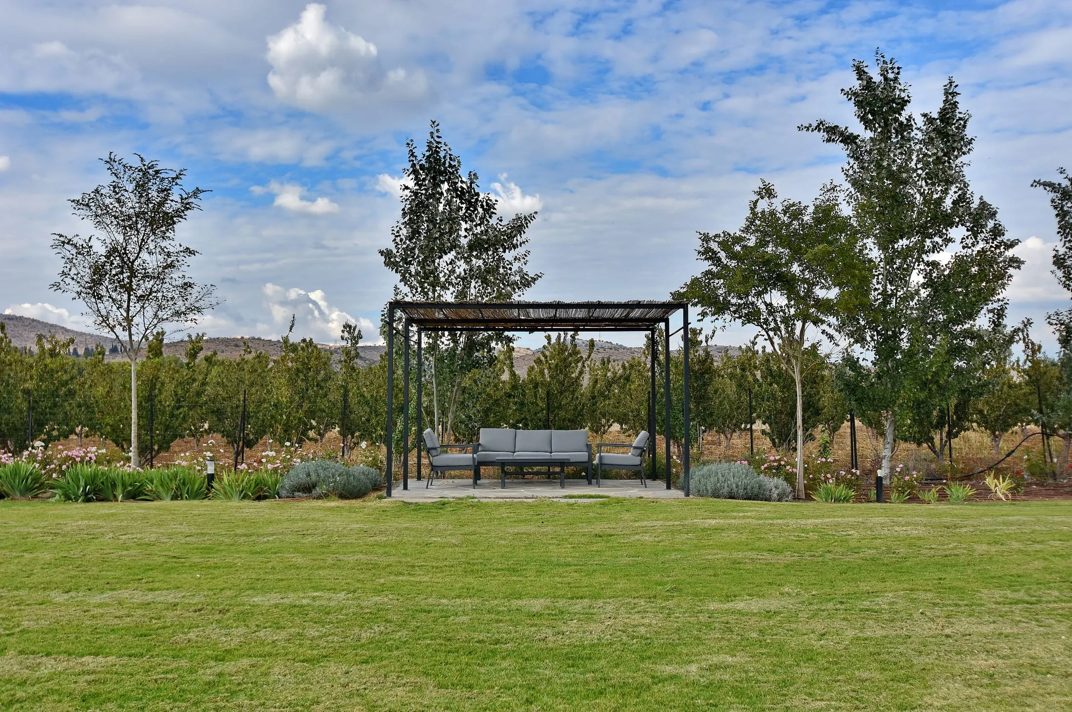 Garden pergola with lounge seating on a wide lawn under a dramatic blue sky